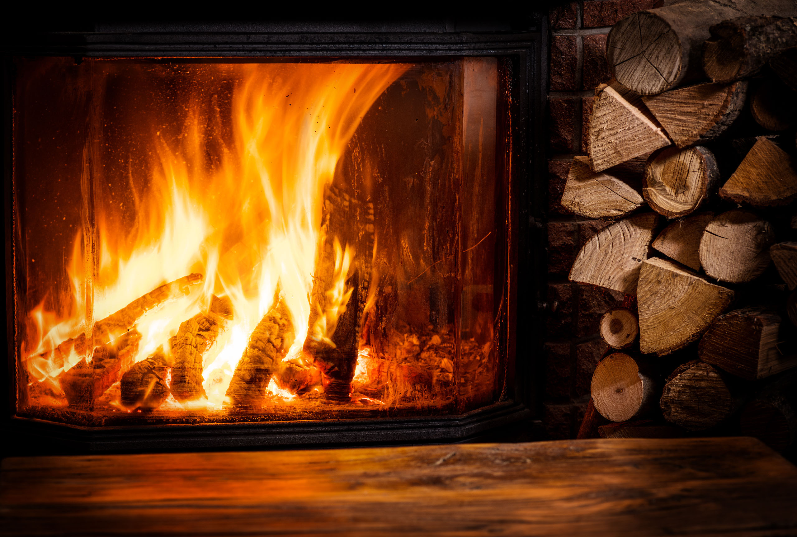 Brennender Kamin mit Holz daneben - Brennholz Jetzinger